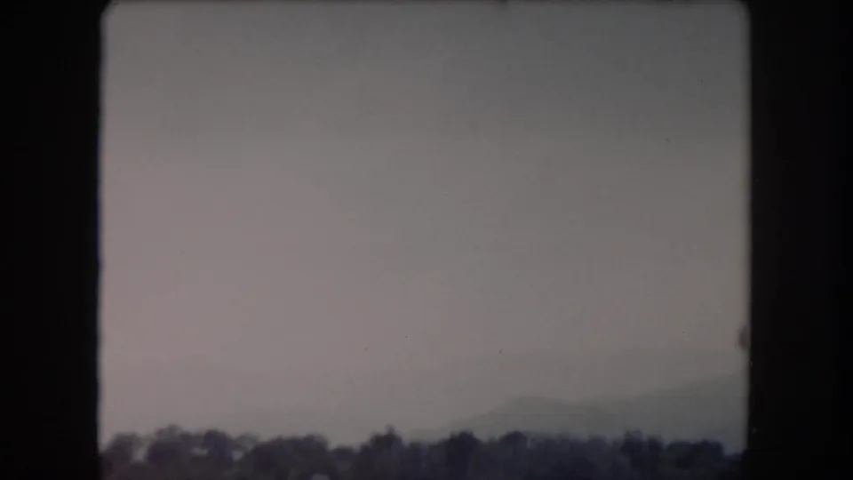 1962 8mm frame from Summit County, Colorado showing a cloudy sky above a distant treeline and a small indistinct object in the air.