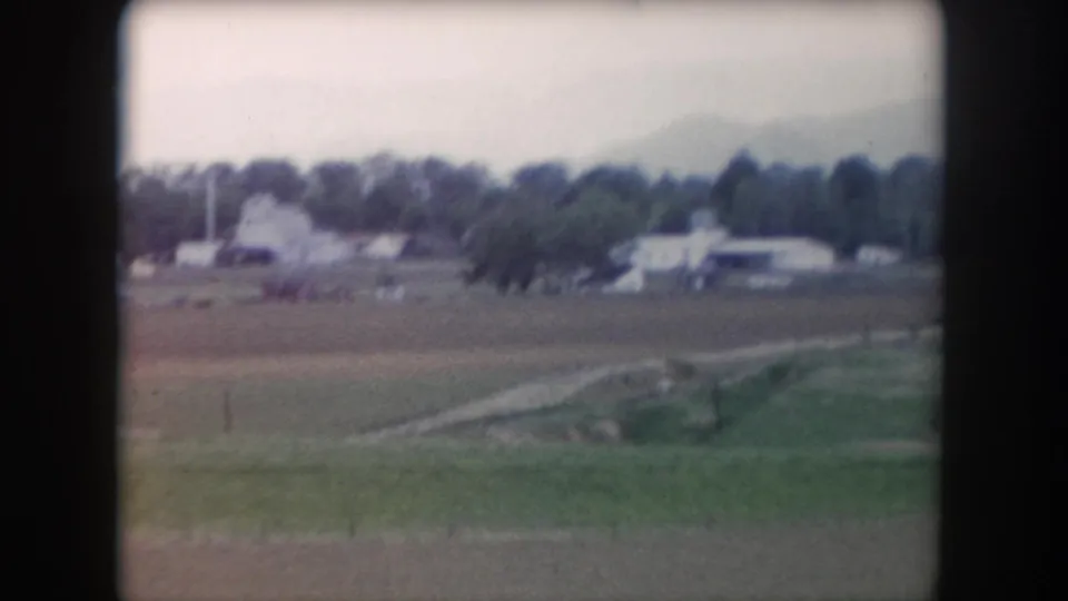 Faded 8mm frame from Summit County, Colorado showing fields, a distant building cluster, trees, and a pale cloudy sky.