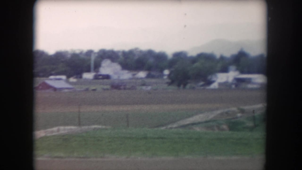 1962 Summit County rural view across fields toward barns, farmhouses, tree line, and distant hazy mountains.