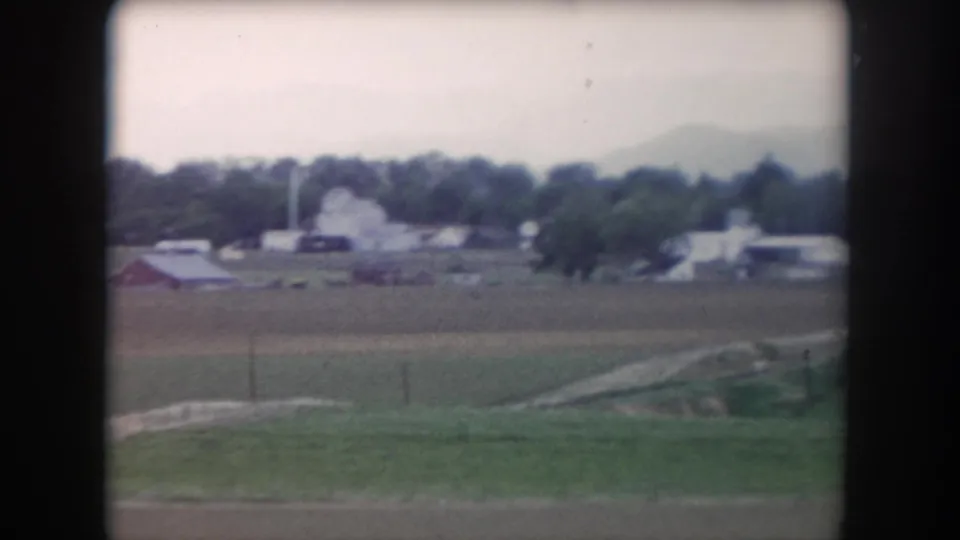 1962 Summit County rural view across fields toward barns, farmhouses, tree line, and distant hazy mountains.