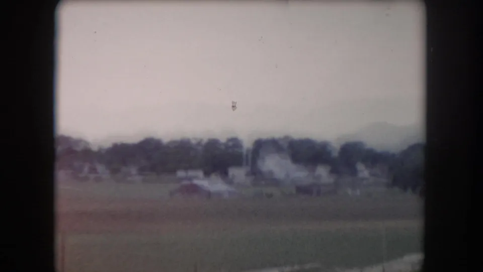 Soft 8mm frame of Summit County fields and farm structures, with trees and distant mountains partly obscured by haze.