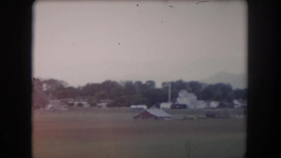 1962 Summit County farmland with a red barn, pale farm buildings, a tree line, fence line, and hazy mountain backdrop.