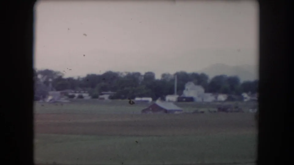 1962 8mm view of a Summit County pasture looking toward distant barns or houses, trees, and a pale morning sky.