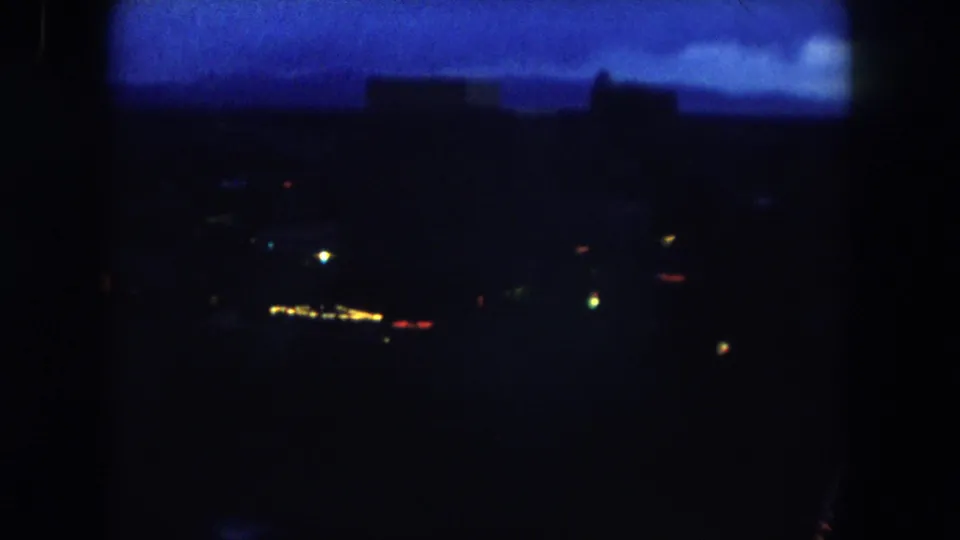 1962 Summit County night view with glowing points of light, a blue horizon, and dark building or hillside silhouettes.