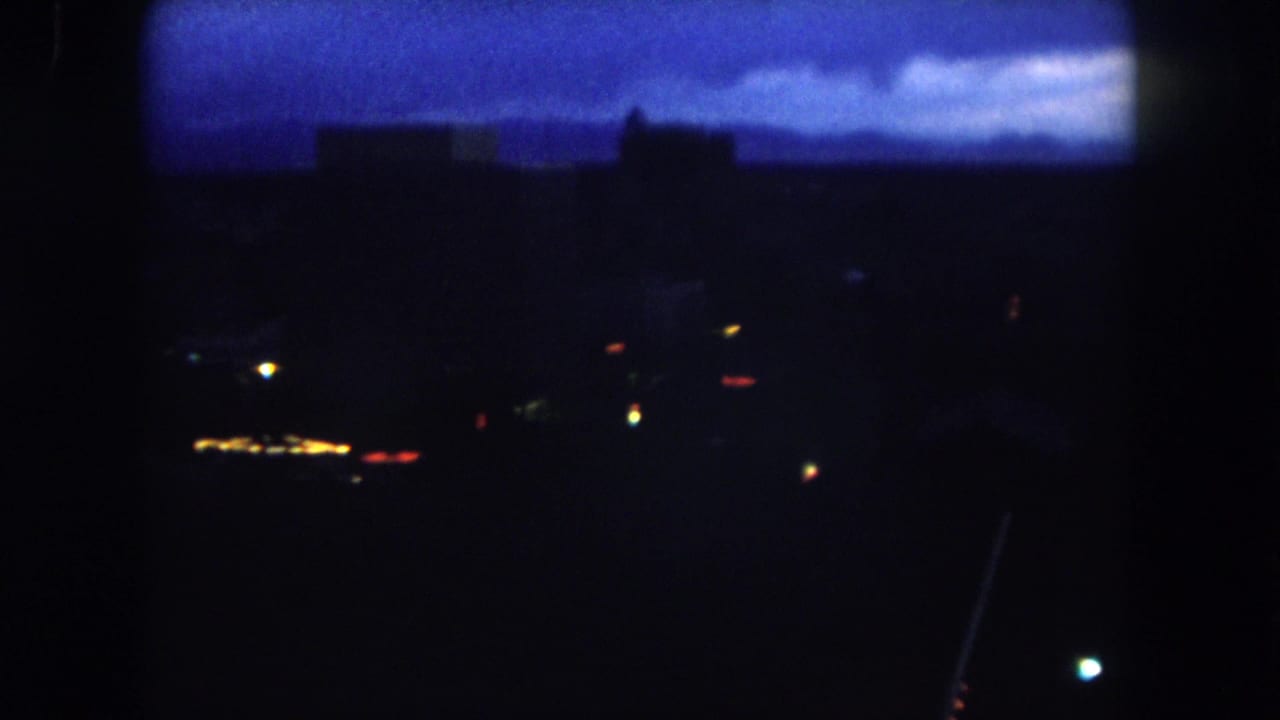 1962 Summit County, Colorado 8mm frame showing a dark distant town or city scene under a blue dawn sky with a few visible lights.