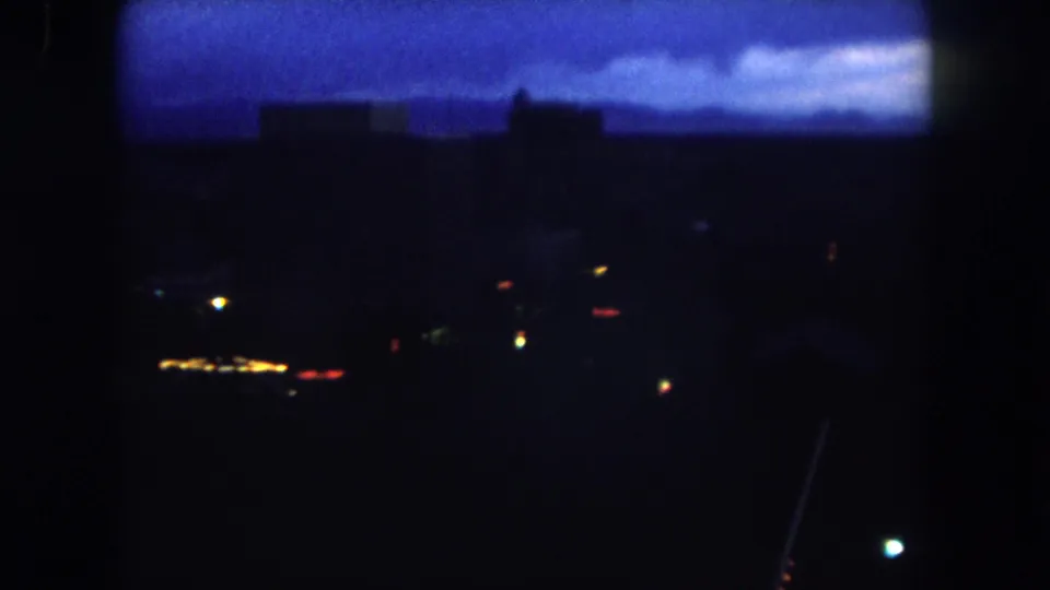 1962 Summit County, Colorado 8mm frame showing a dark distant town or city scene under a blue dawn sky with a few visible lights.
