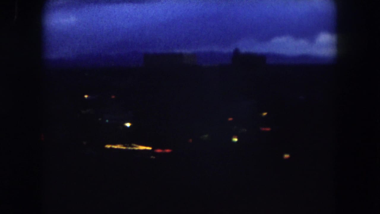 Blue dawn clouds over a mostly dark town or city with scattered points of light.