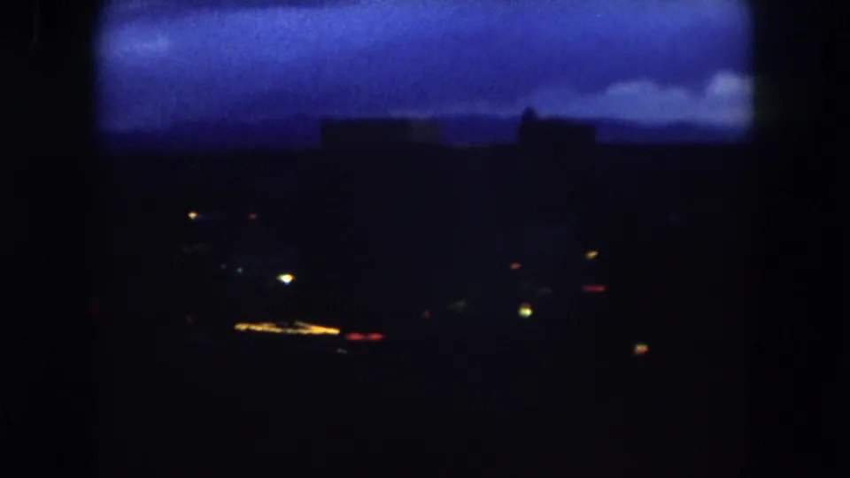 1962 Summit County, Colorado frame with a dark low skyline, blue cloud band, and scattered town lights in soft 8mm focus.