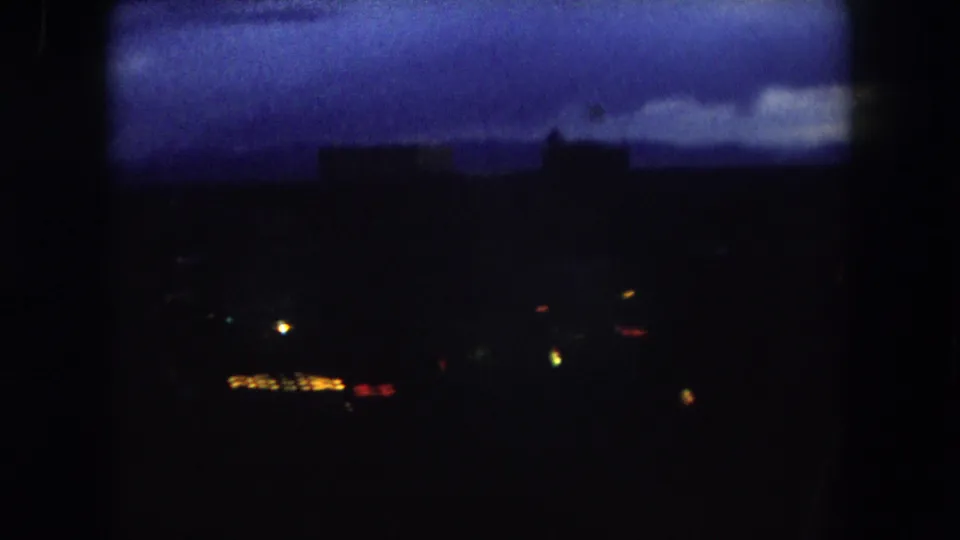 1962 Summit County, Colorado 8mm view of a dark town scene with faint building shapes, warm lights, and a blue dawn cloud layer.