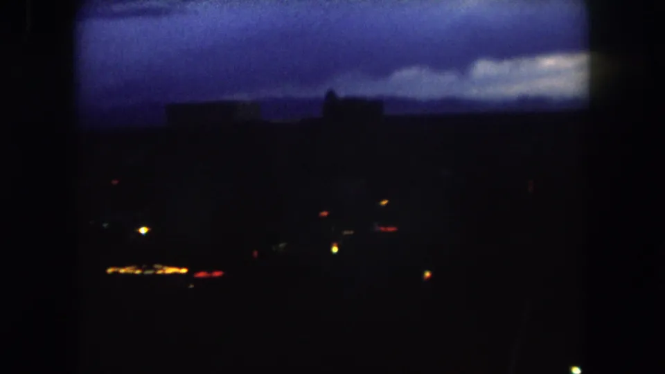 1962 Summit County, Colorado frame showing the pan continuing across a dark town or city view with scattered lights and a blue-purple sky.