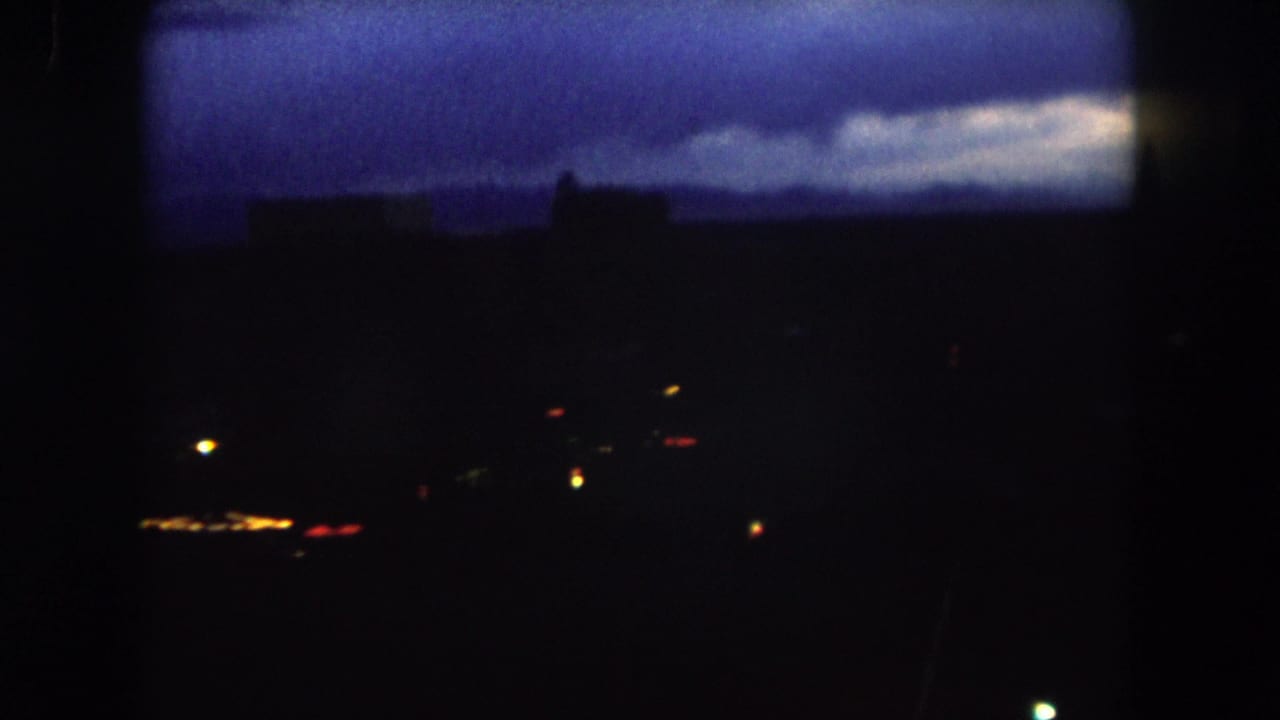 1962 Summit County, Colorado home-movie frame showing a dark town skyline, scattered lights, and a blue twilight sky.