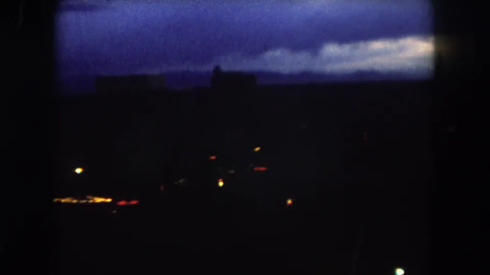 1962 Summit County, Colorado home-movie frame showing a dark town skyline, scattered lights, and a blue twilight sky.