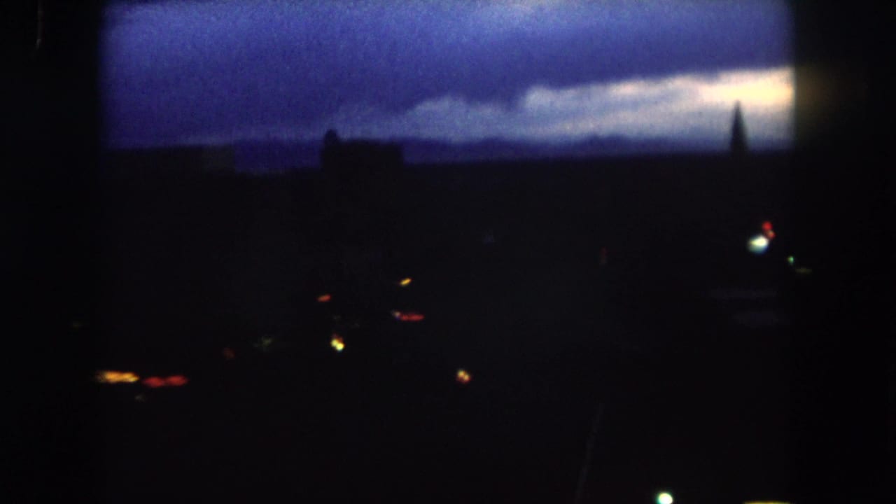 1962 Summit County, Colorado frame with silhouetted structures, a narrow spire-like form, and small lights at dusk.