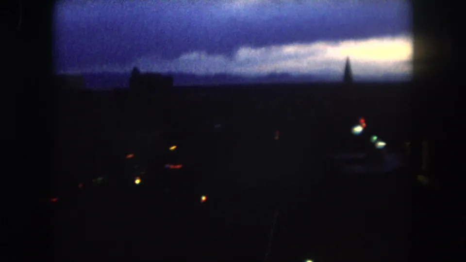 1962 Summit County, Colorado home-movie frame showing a dark town overview, bright dusk horizon, and scattered street or building lights.
