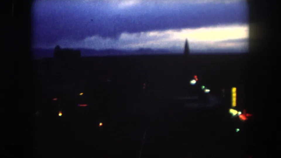 1962 Summit County, Colorado frame showing a dark skyline, scattered colored lights, and a vertical illuminated sign-like shape at dusk.