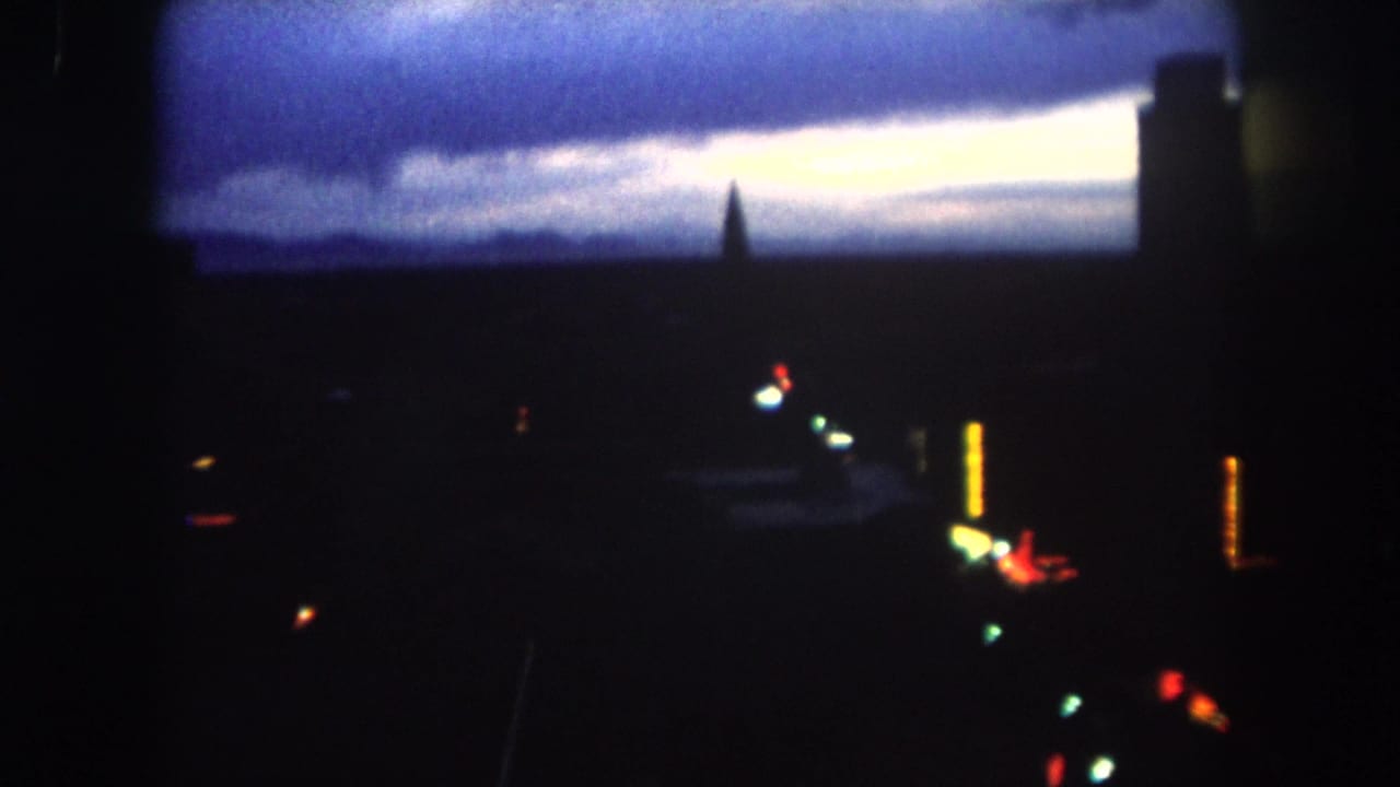 Low-light skyline with blue clouds, a bright horizon strip, building silhouettes, and small colored lights.