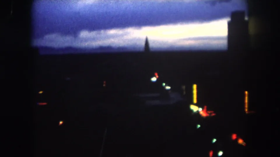 Dark Summit County, Colorado dawn skyline on 8mm film, showing a blue cloud layer, pale horizon, silhouetted structures, and scattered lights.