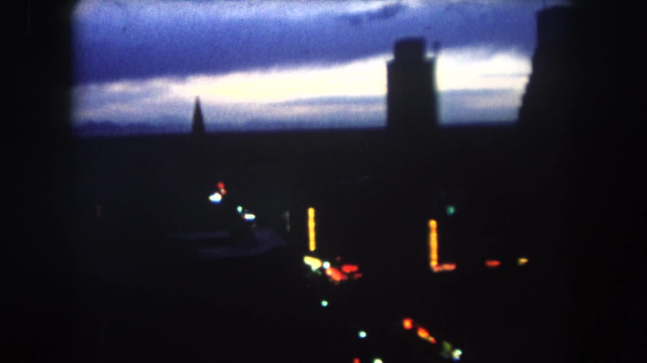 1962 Summit County, Colorado 8mm frame showing silhouetted towers and scattered city lights under a cloudy twilight sky.