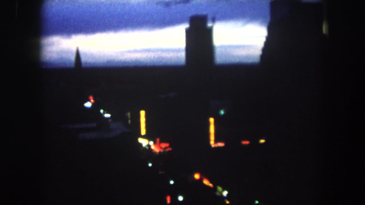 Low-light 8mm view of Summit County at dusk, with silhouetted structures, a tower form, and blurred street or building lights.