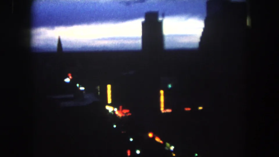 Low-light 8mm view of Summit County at dusk, with silhouetted structures, a tower form, and blurred street or building lights.