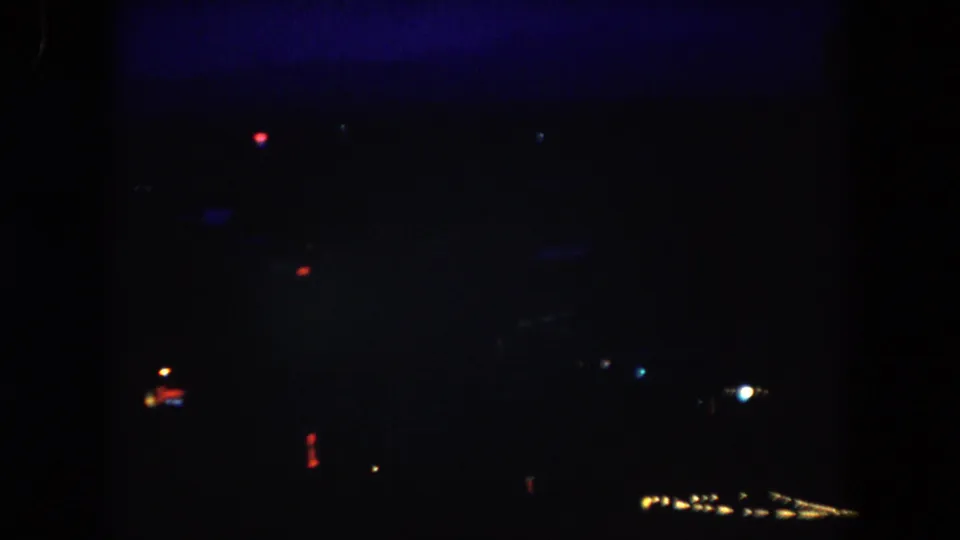 Underexposed 1962 home-movie frame from Summit County, showing sparse colored lights against a mostly dark evening view.