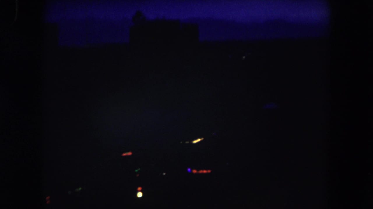 1962 Summit County, Colorado 8mm frame showing a very dark elevated night view with faint horizon silhouettes and a few blurred city lights.