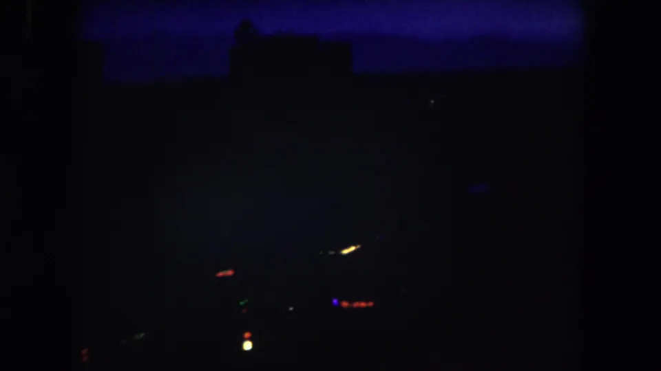 1962 Summit County, Colorado 8mm frame showing a very dark elevated night view with faint horizon silhouettes and a few blurred city lights.