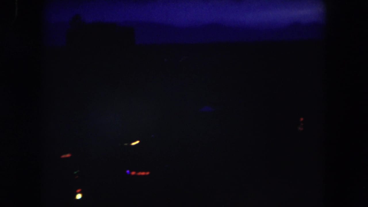 Dark 8mm night view from Summit County, Colorado, with a blue horizon band, indistinct structures, and sparse blurred lights in the distance.
