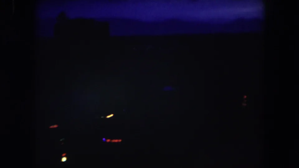 Dark 8mm night view from Summit County, Colorado, with a blue horizon band, indistinct structures, and sparse blurred lights in the distance.