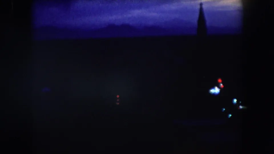 Summit County 1962 night frame showing a blue-black horizon, a possible steeple-like silhouette, and a few bright blurred lights at right.