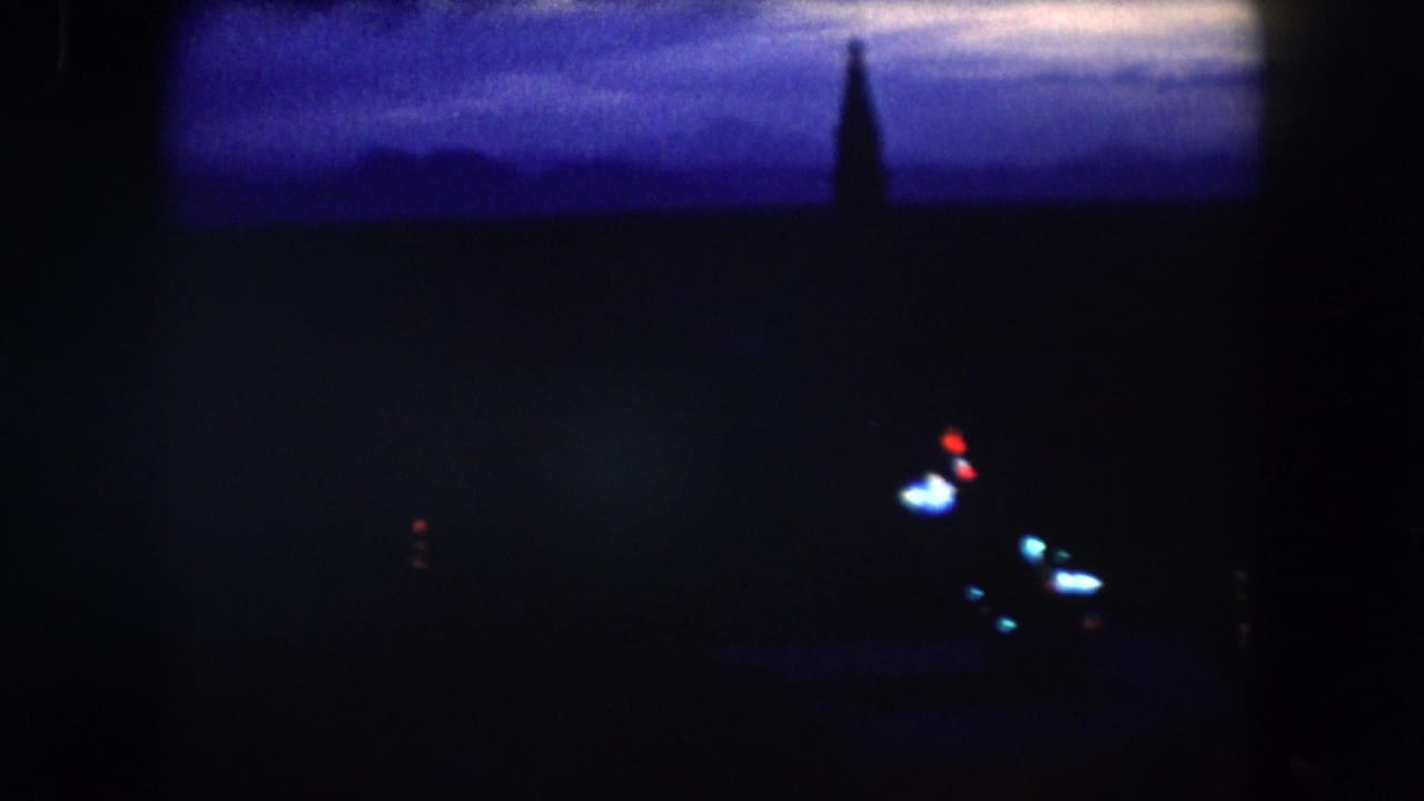 1962 8mm nighttime descent view over Summit County, Colorado, with blue twilight, sparse lights, and a dark spire shape.