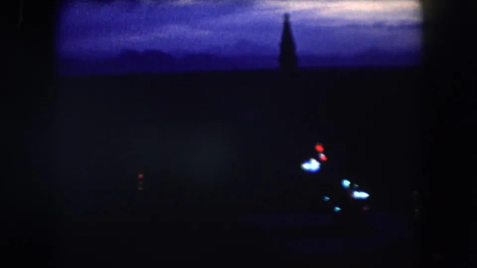 1962 8mm nighttime descent view over Summit County, Colorado, with blue twilight, sparse lights, and a dark spire shape.
