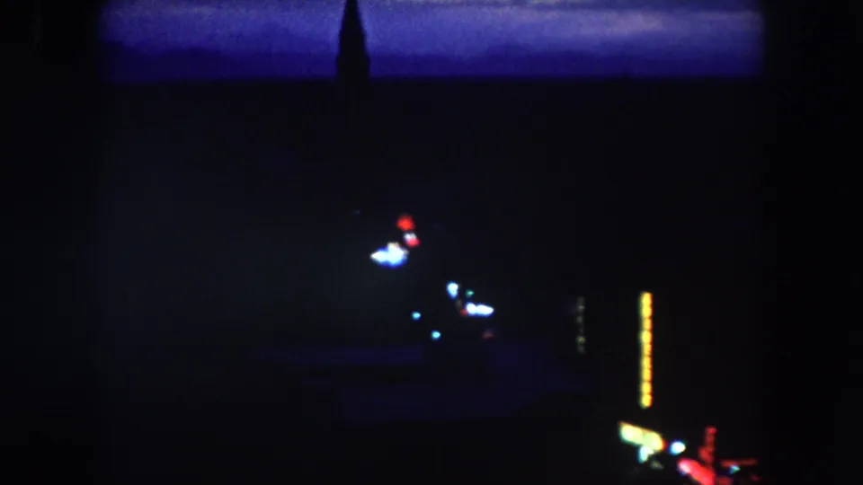 A dark 1962 Colorado descent frame shows sparse city lights, a silhouetted spire, and bright vertical illuminated sign shapes.