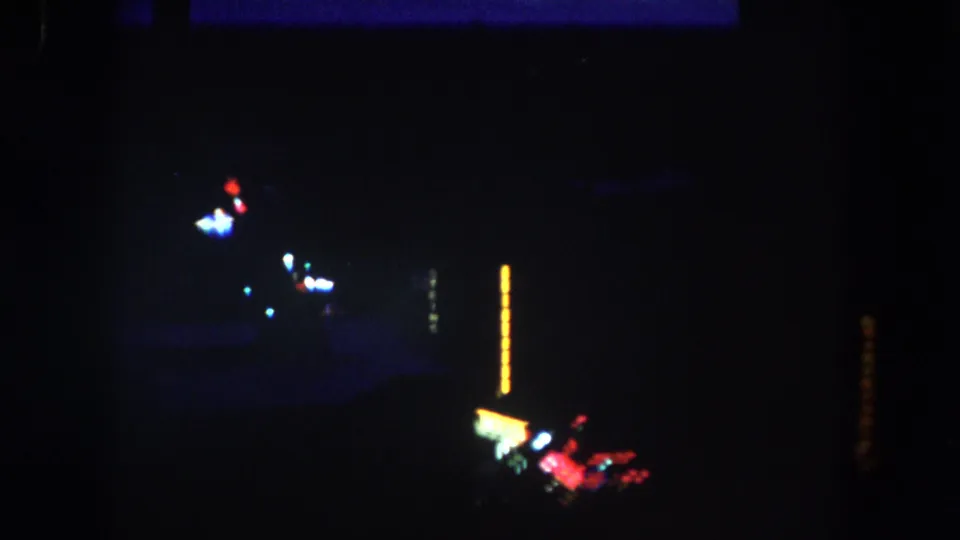 Nighttime 8mm descent view in Summit County, Colorado, with underexposed town lights and bright sign glow near the bottom of frame.