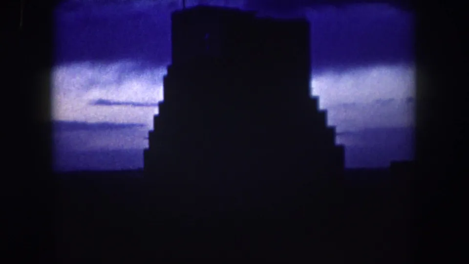 Low-light 1962 home-movie frame from Summit County with a dark building outline and blue sky behind it.