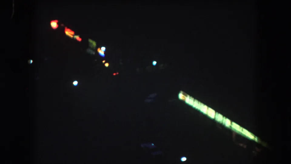 1962 Summit County night exterior with scattered small lights, deep shadows, and a bright green illuminated sign-like band at right.