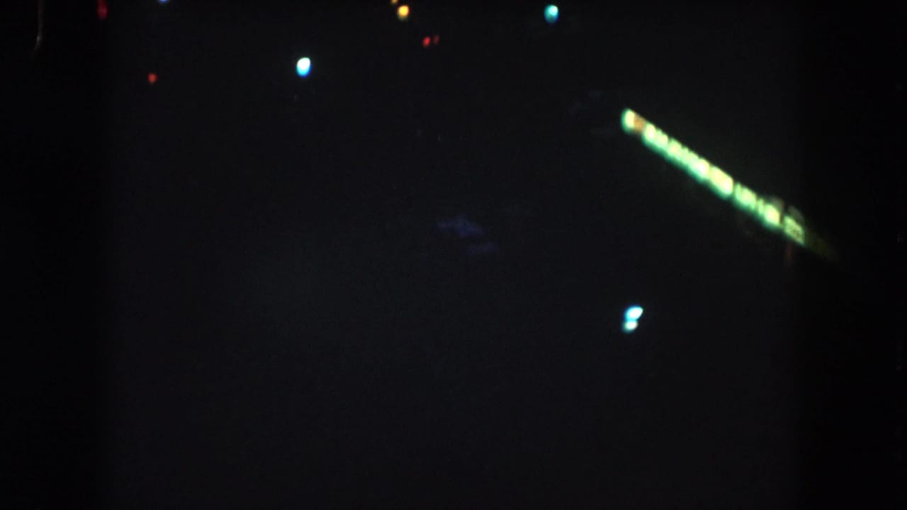 Dark aerial night view with scattered colored lights and a diagonal green streak.