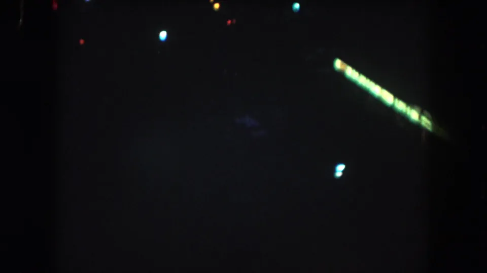 1962 Summit County home-movie frame showing a dark nighttime aerial view with scattered lights and a diagonal green light streak.