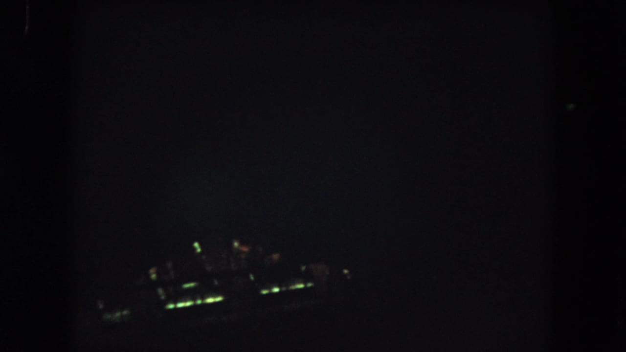 Dark 8mm night aerial frame from the Summit County clip with a small blurred cluster of greenish lights visible below.