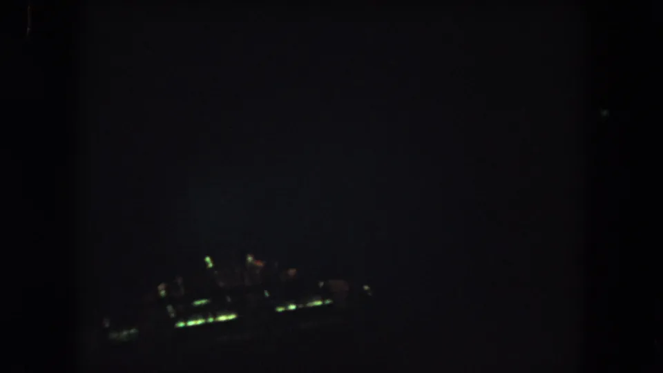Dark 8mm night aerial frame from the Summit County clip with a small blurred cluster of greenish lights visible below.