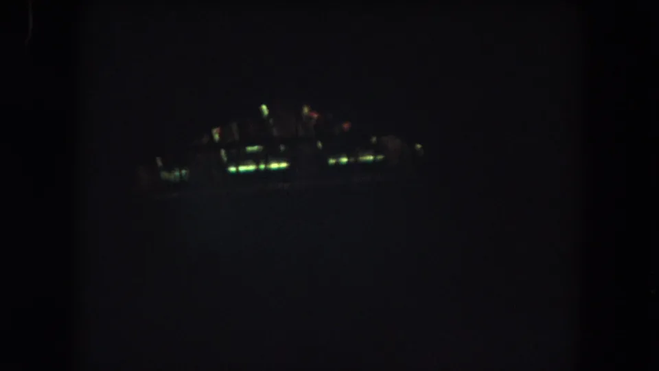 1962 Colorado night-flight frame showing a blurred illuminated cluster against a largely black 8mm film background.