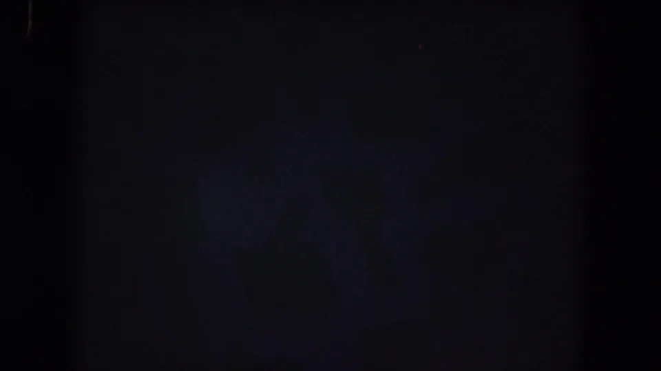 Underexposed 8mm frame from the 1962 clip, showing mostly dark foreground or leader-like texture with no clear people visible.