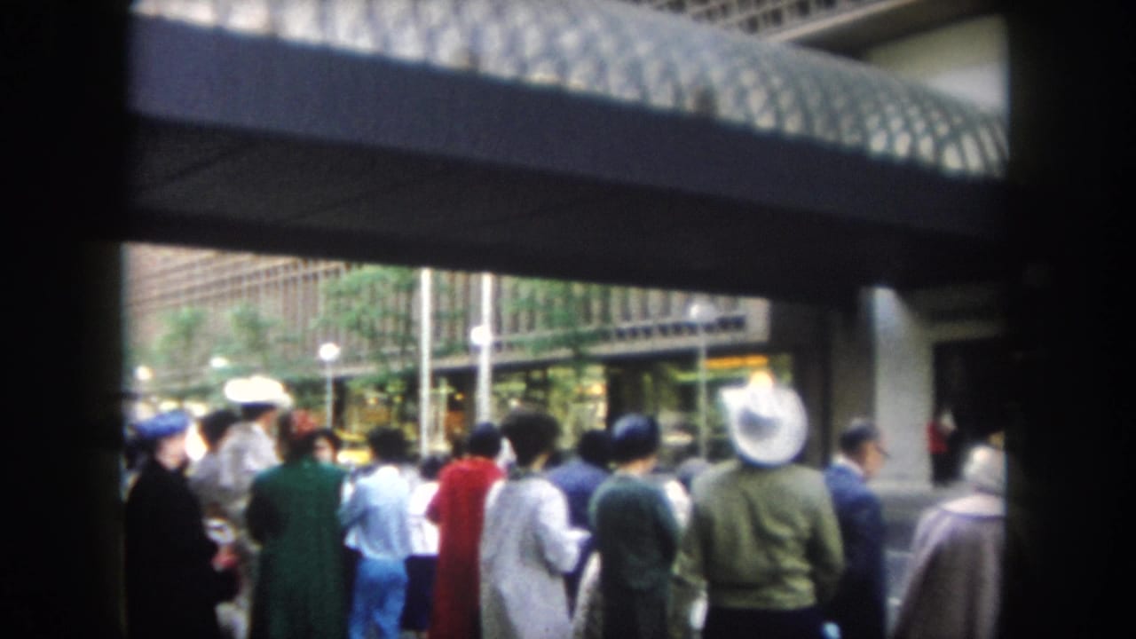 People in mid-century clothing wait and face toward an entrance in this Summit County, Colorado 8mm frame.