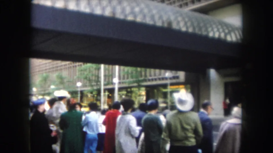 People in mid-century clothing wait and face toward an entrance in this Summit County, Colorado 8mm frame.