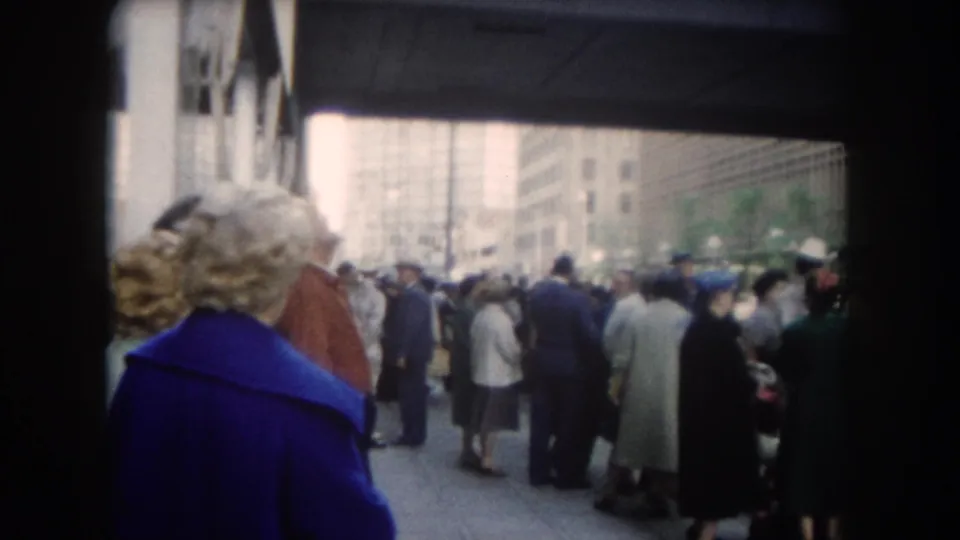 Close 8mm view of a 1962 Colorado-labeled city sidewalk crowd, with the camera positioned behind onlookers in coats.