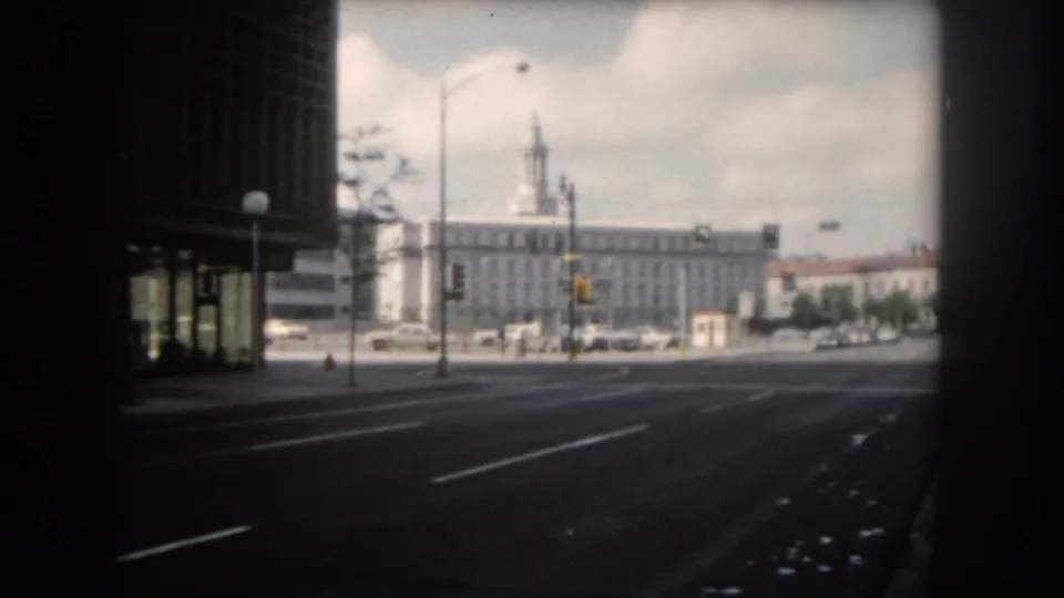 1962 Colorado-labeled street view showing open traffic lanes, cars, tall buildings, and a clock-tower building in the background.