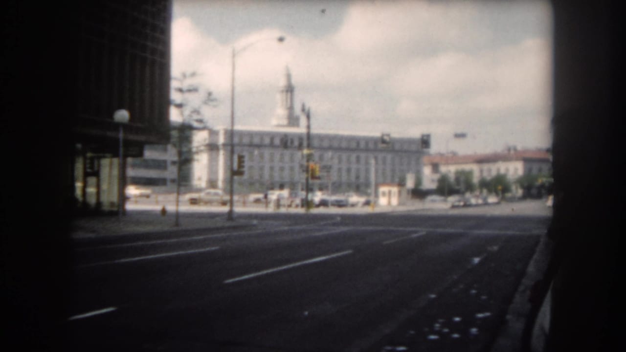 Wide road with lane markings, traffic lights, parked cars, and a light building in the distance.