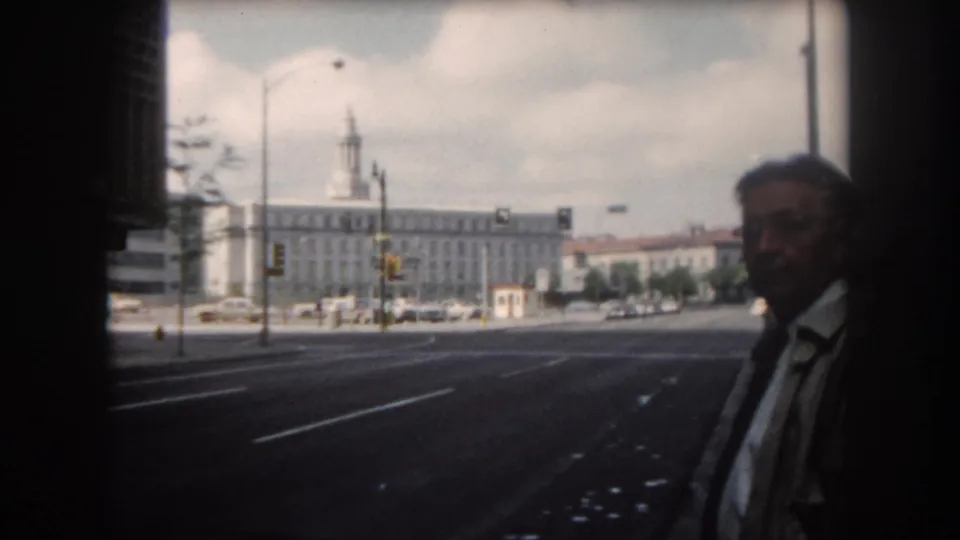 Adult man in a light jacket, white shirt, and dark tie appears close to the camera in a 1962 Summit County street scene.