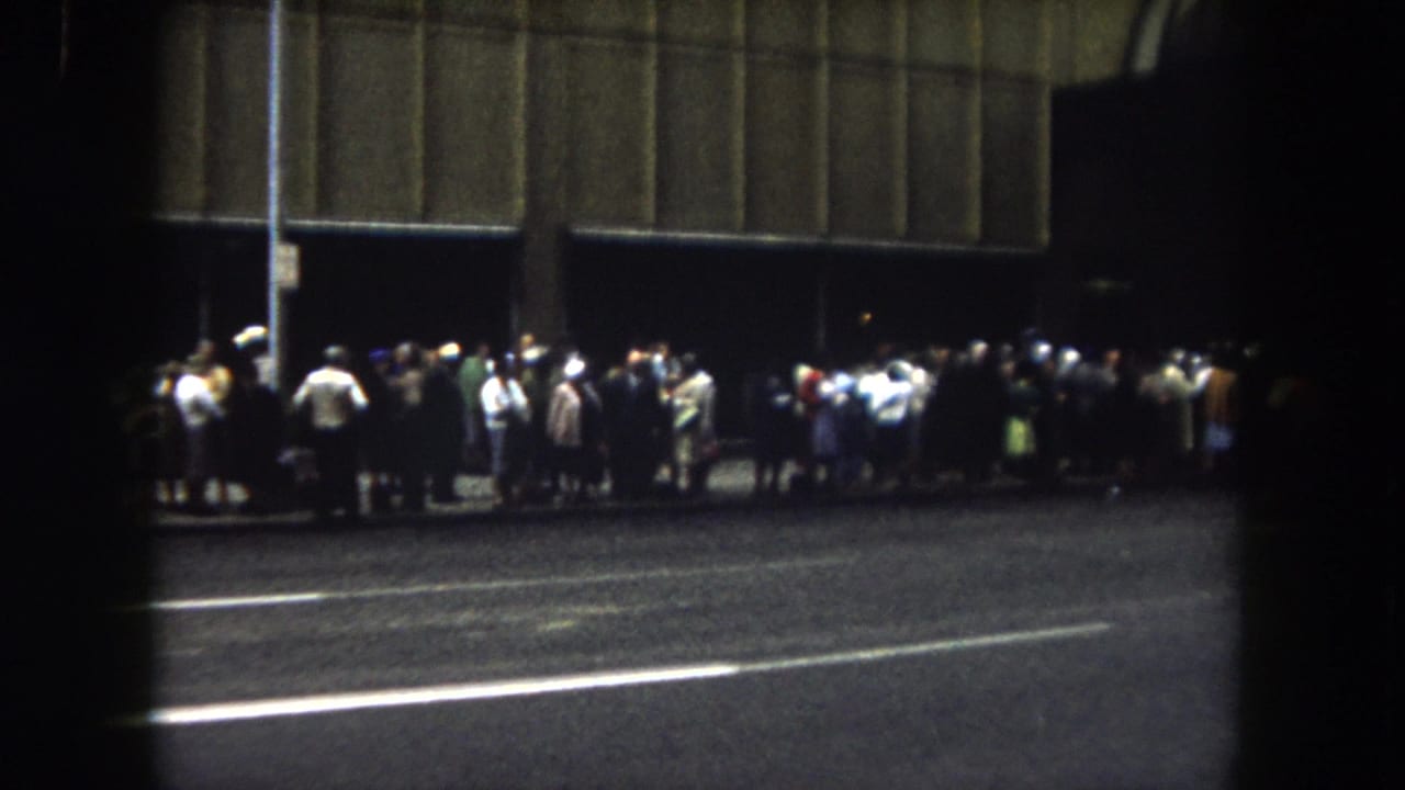 1962 Summit County, Colorado 8mm frame showing a nighttime curbside crowd gathered beside a large shadowed facade.