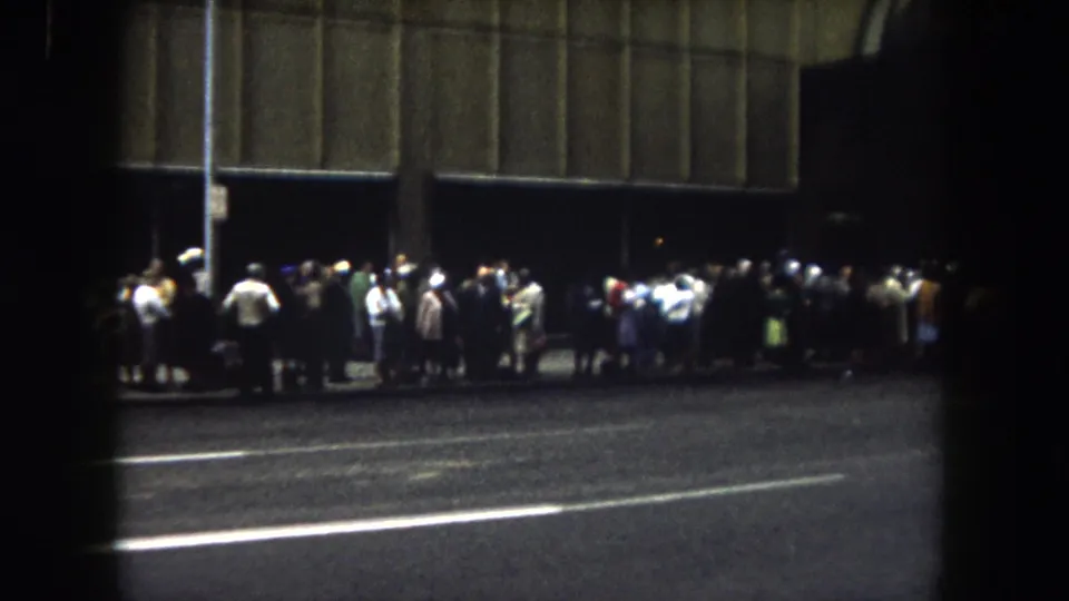 1962 Summit County, Colorado 8mm frame showing a nighttime curbside crowd gathered beside a large shadowed facade.